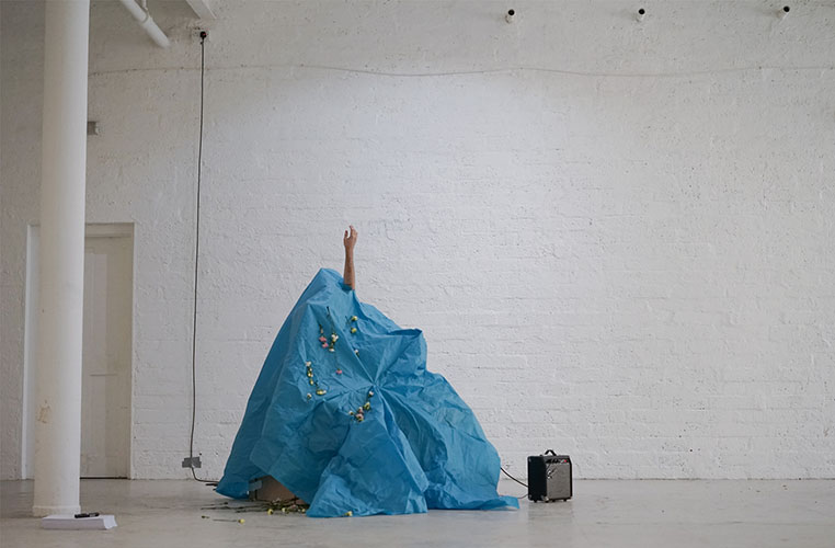 Performance artist under a Blue Plastic sheet with arm aloft